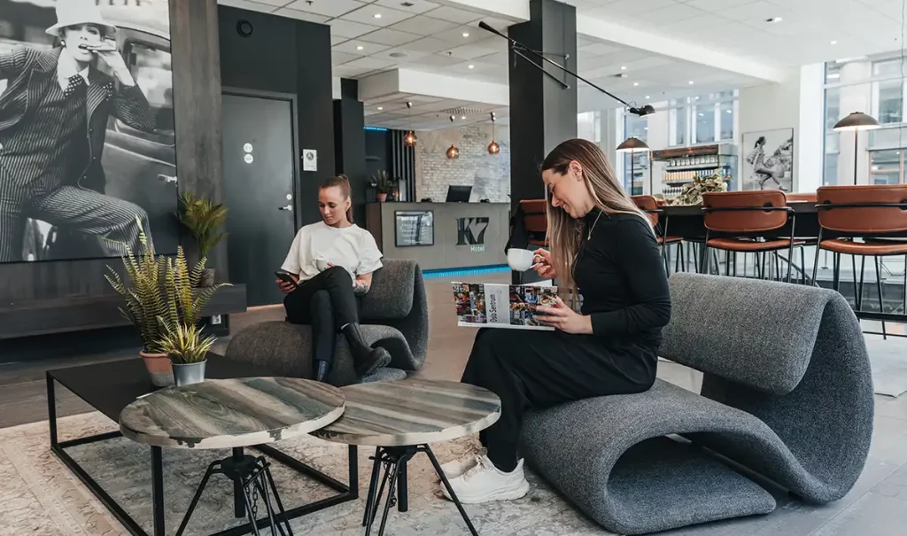 Two women sitting in the lobby of K7 Hotel Oslo, drinking coffee and reading.