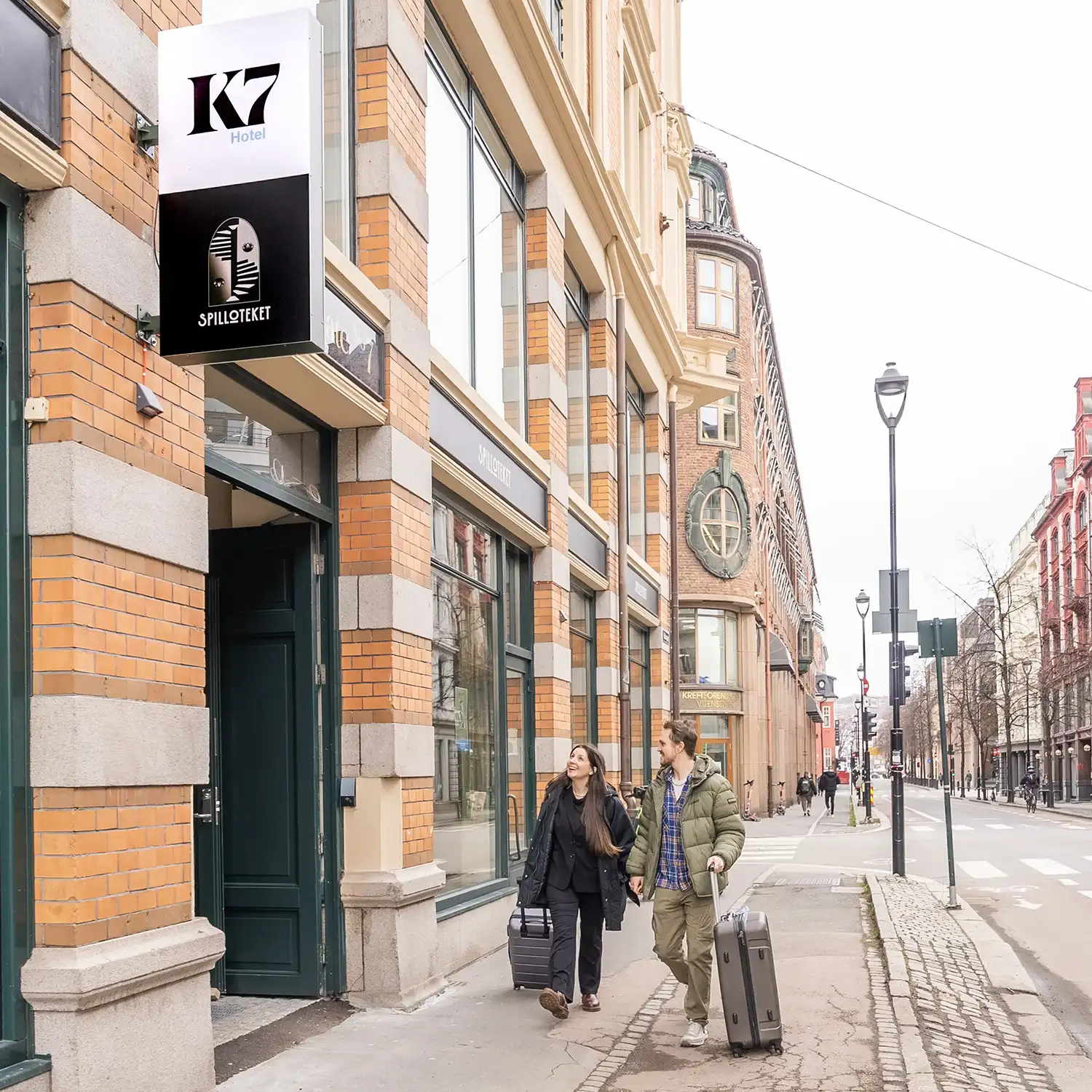 Couple with suitcases walking towards entrance of K7 Hotel Oslo