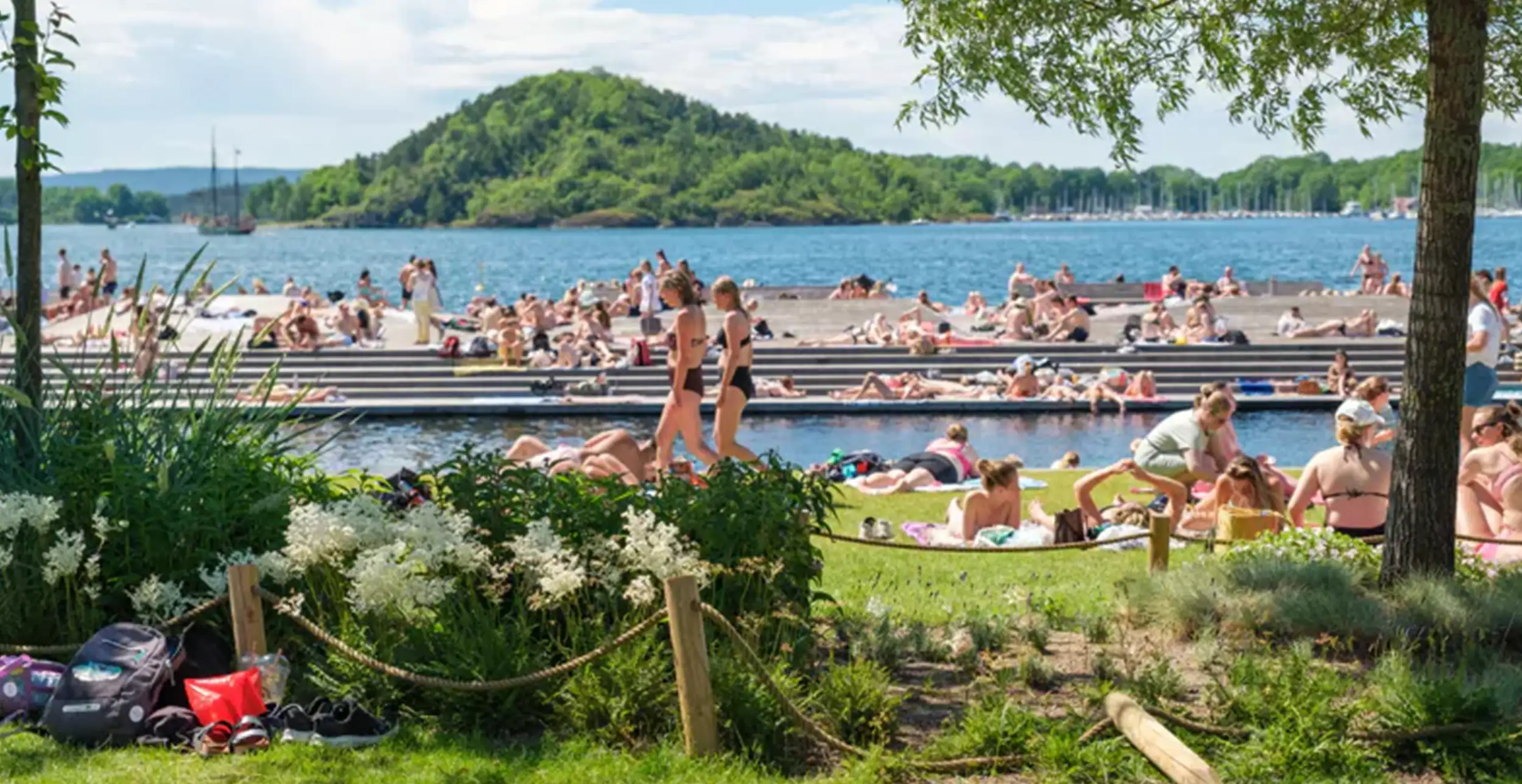 People sitting on the grass with Sørenga Sjøbad in the background. Photo by: Nikolai Kobets Freund / Oslo kommune